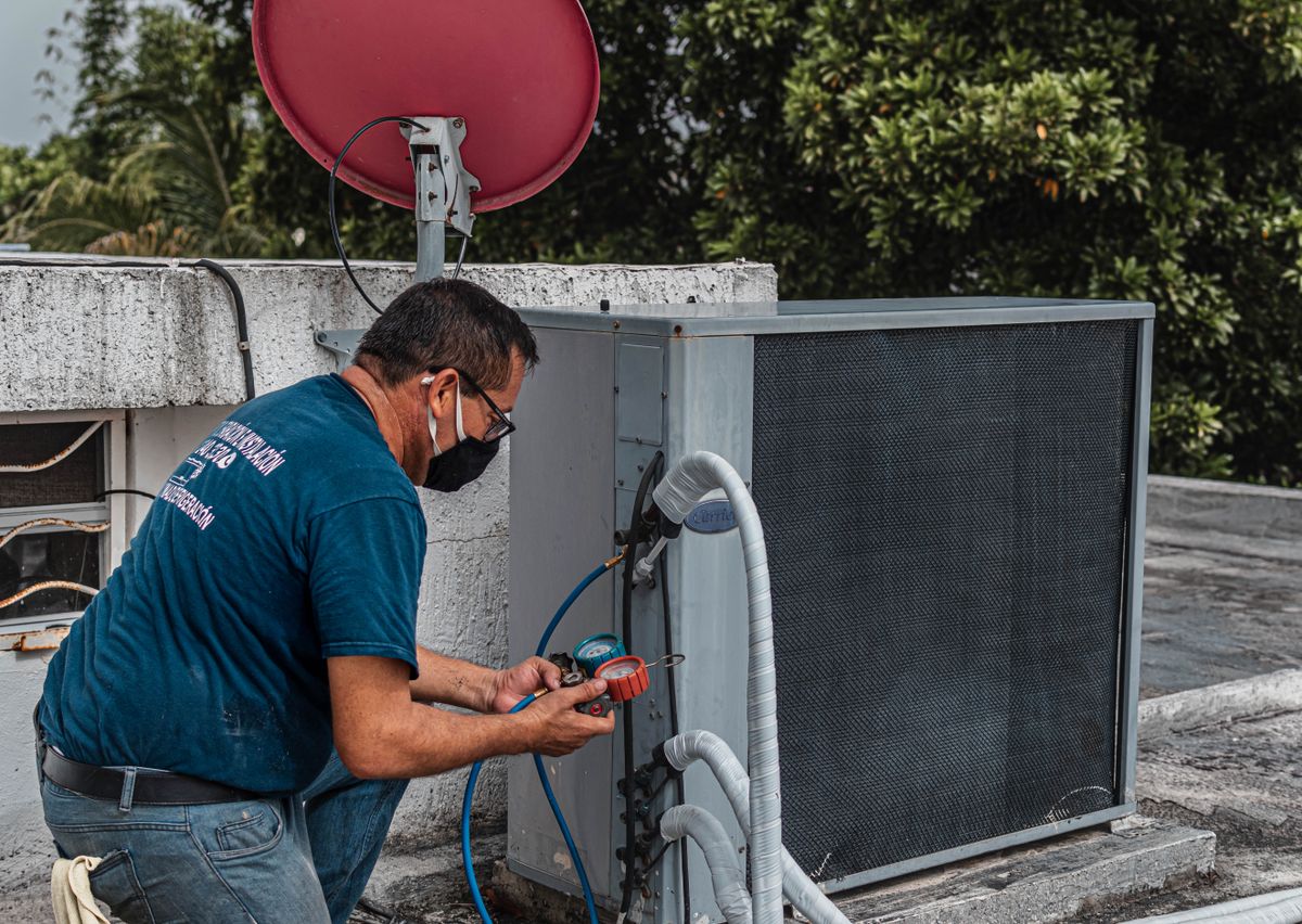 A technician servicing an air conditioning unit with a manifold gauge